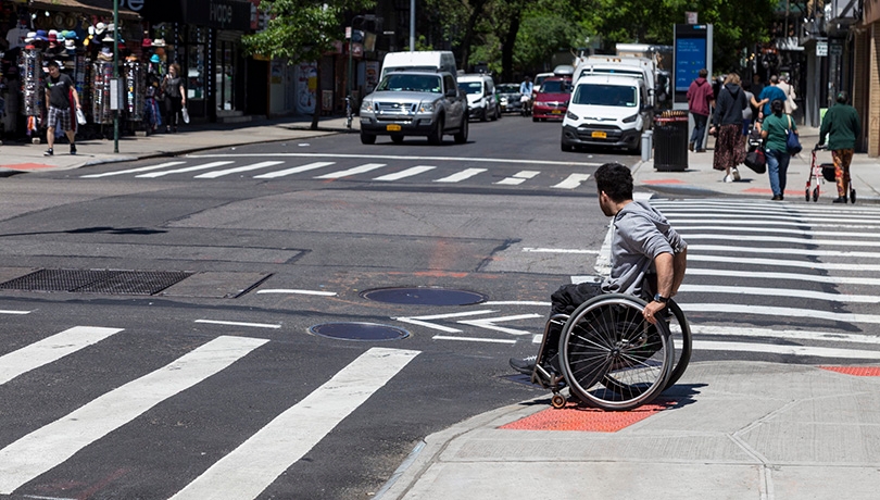 Man in a wheelchair going down a pedestrian ramp