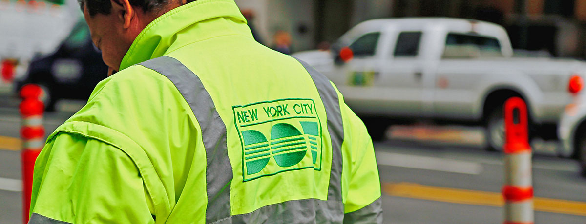 The back of a man wearing a neon green N Y C D O T jacket.