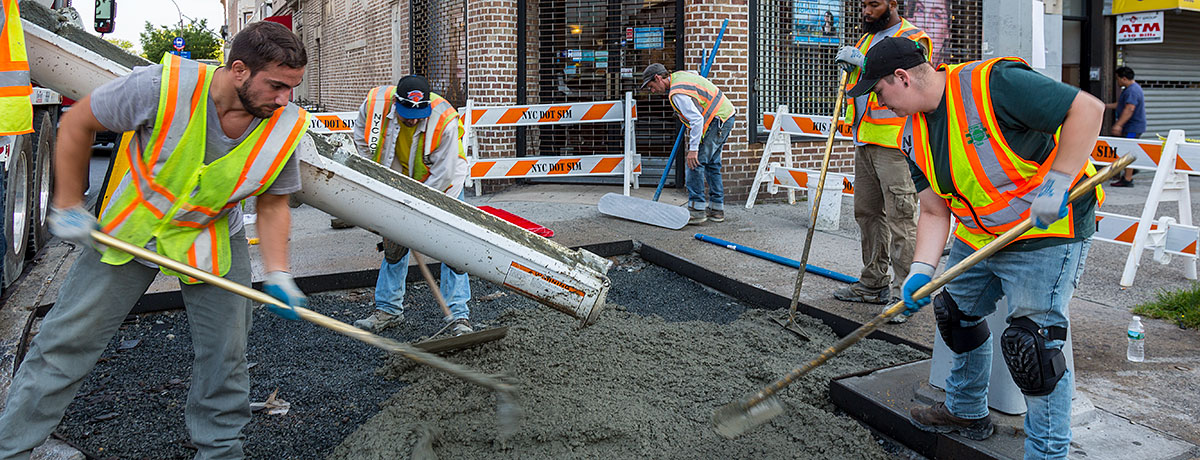 N Y C D O T construction workers leveling out fresh concrete to build a new sidewalk corner.