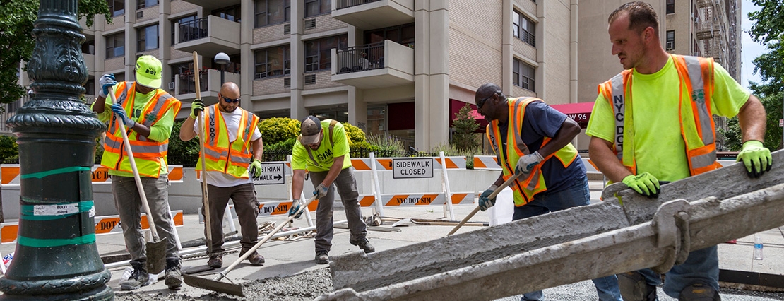 N Y C D O T construction workers laying fresh concrete to build a new sidewalk corner. 